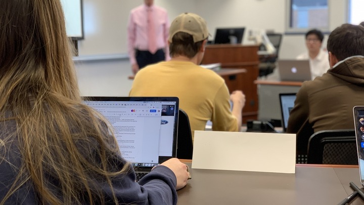 Students with laptops in a classroom facing professor