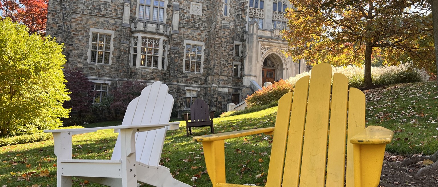 Linderman Library in the fall. There are two Adirondack chairs in the foreground near trees. One is white, the other is yellow