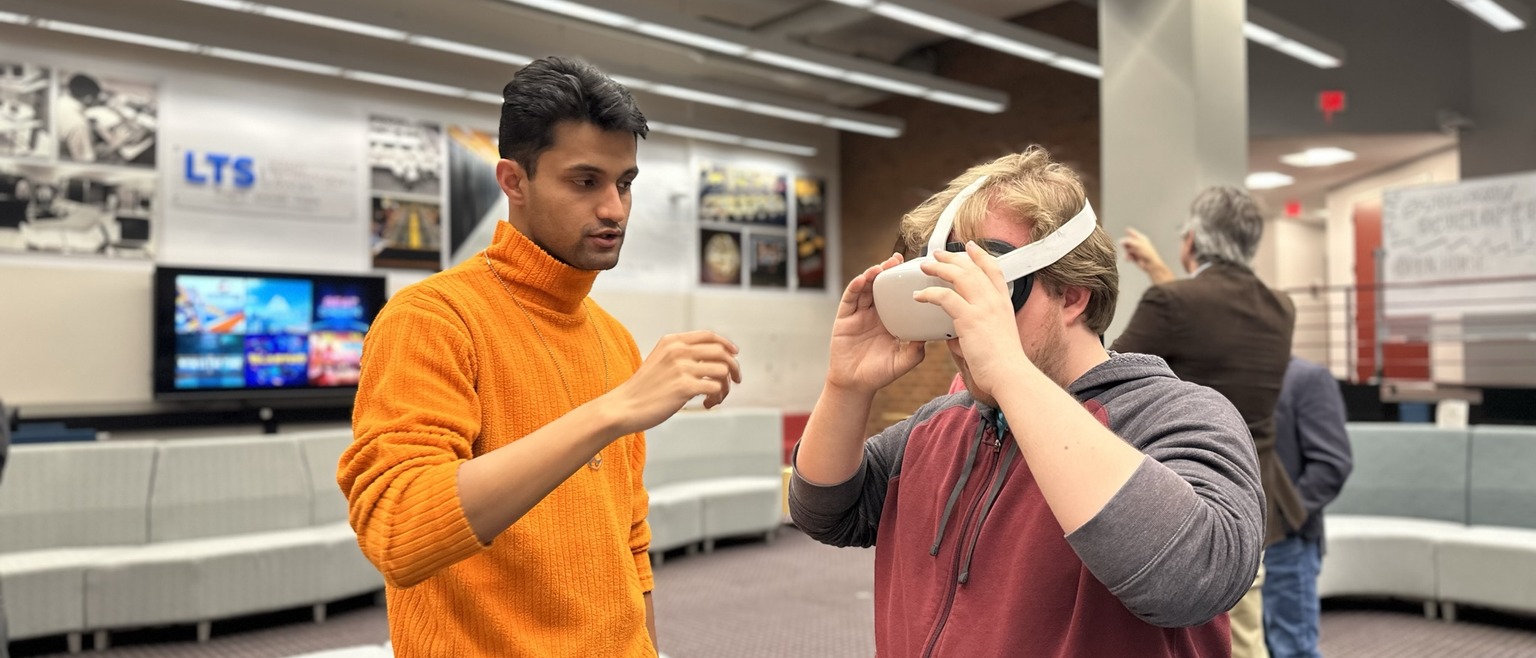 Graduate student assists another student with VR equipment at Student Developer Lab Open House